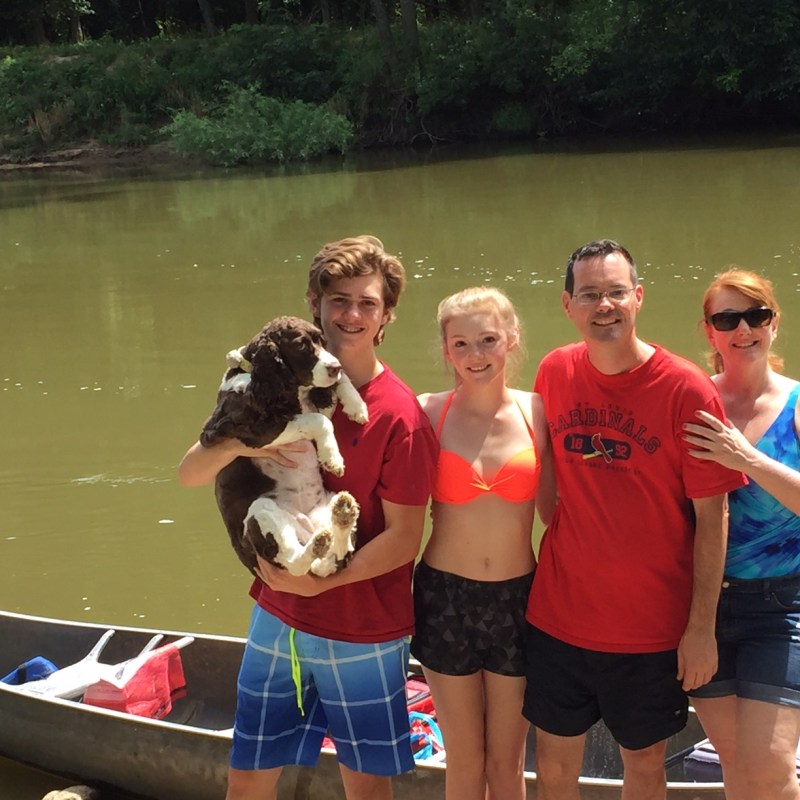 A family with their dog smiling in front of a canoe
