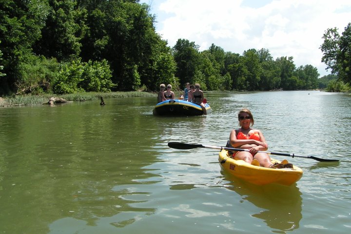 A lady in a kayak and a family enjoying a raft float on the river